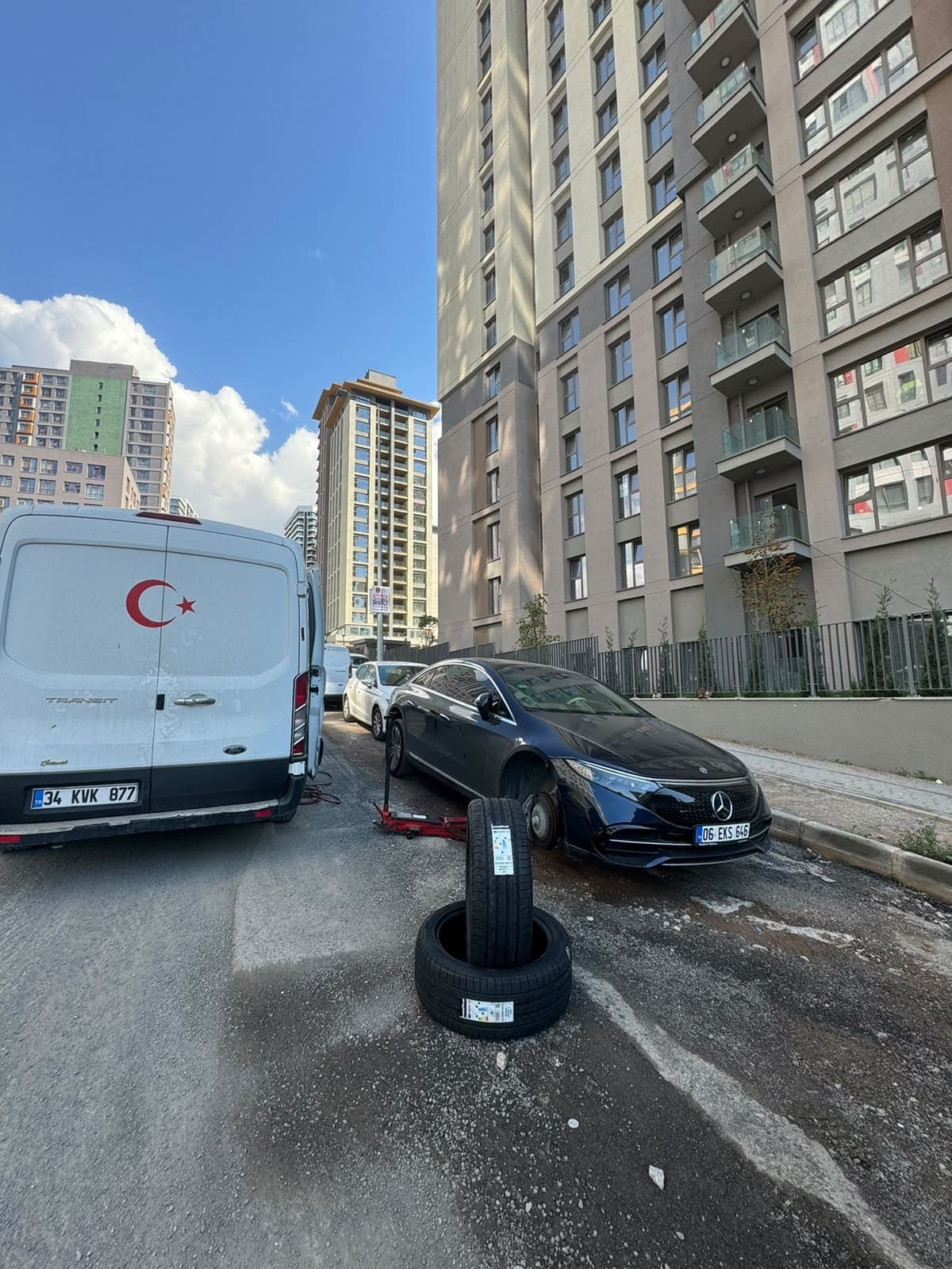 Ön tekerleği sökülmüş otomobilin yanında lastikler ve mobil servis aracı
